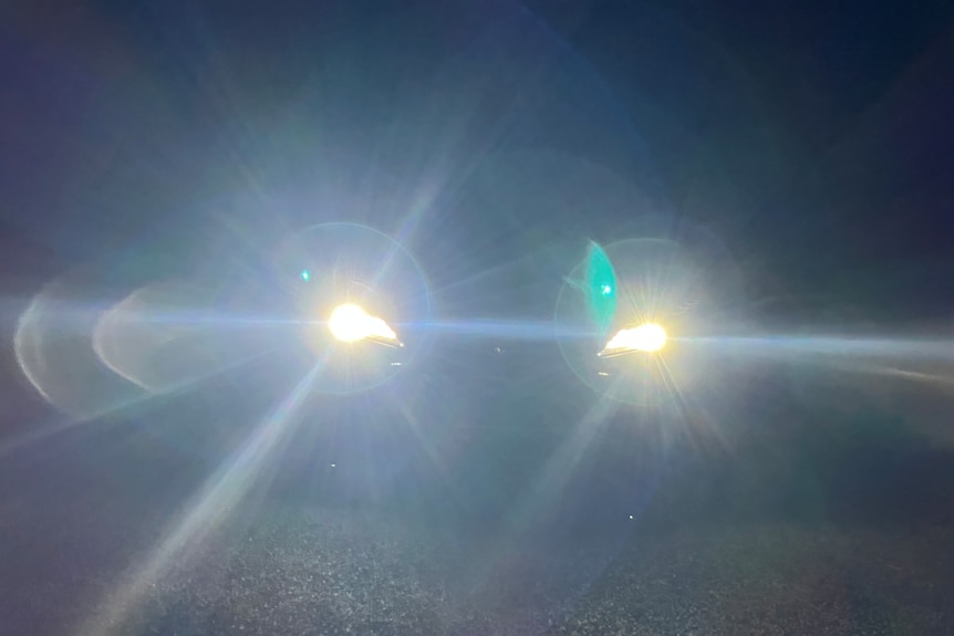 Glare caused by twin headlamps on a road at night.