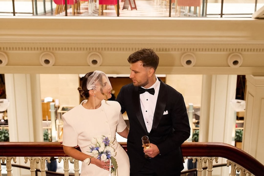 A man and woman in wedding clothing looking at each other on balcony.
