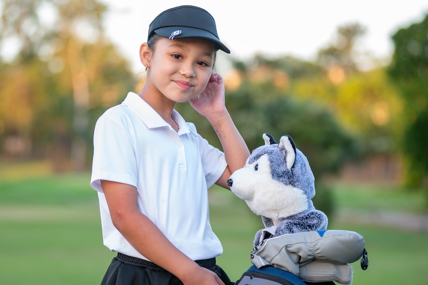 A young girl with a golf bag in front of a golf course.