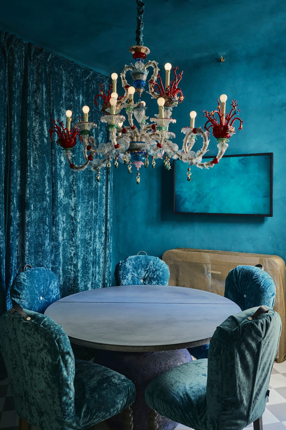 Luxuriously styled dining area featuring a blue theme, velvet chairs, and an ornate chandelier.