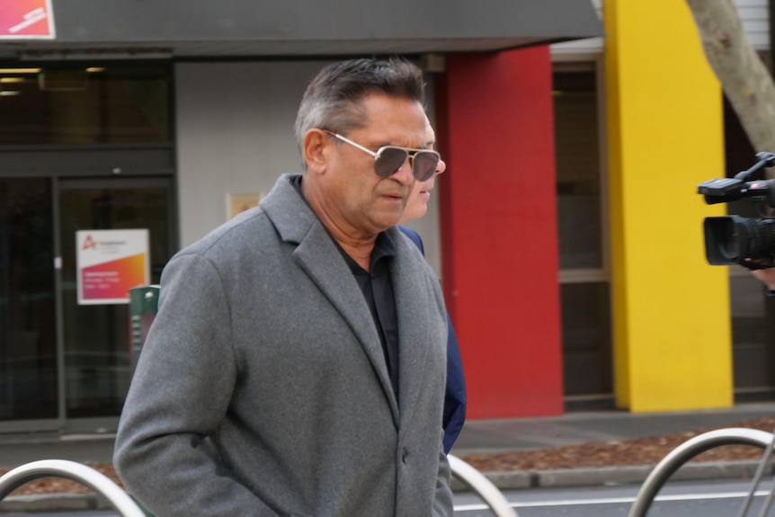 Nicky wearing a grey coat and sunglasses.