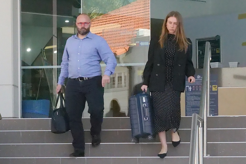 Three people, one male, two females, all holding paperwork and suitcases, walking down steps, dressed professionally