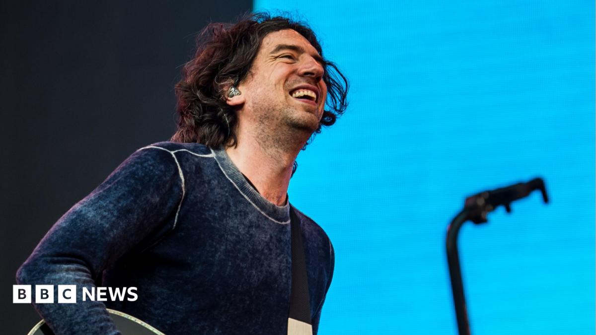 Gary Lightbody of Snow Patrol smiles as he performs on stage at the Latitude Festival in 2025, against a light blue backdrop