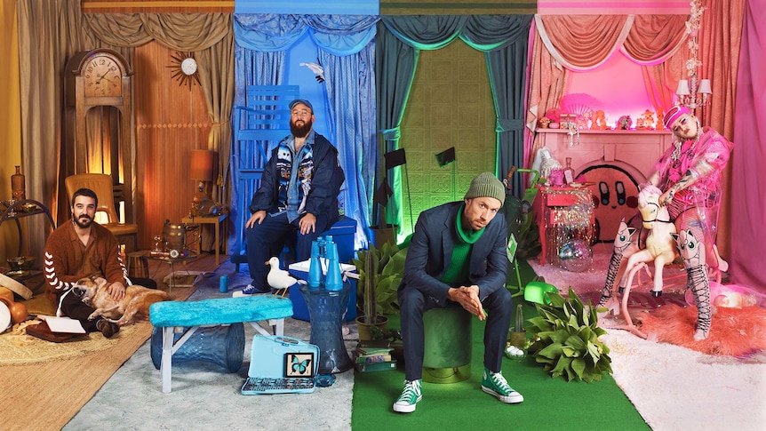 Three men and a women sit in an elaborate set themed in four different colours.