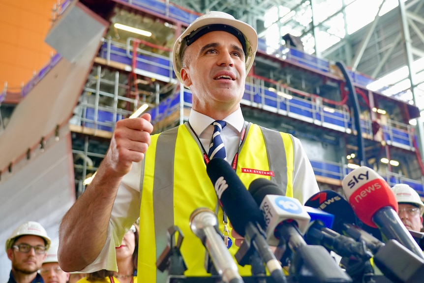Man with fluro vest and hard hat speaking on a microphone.