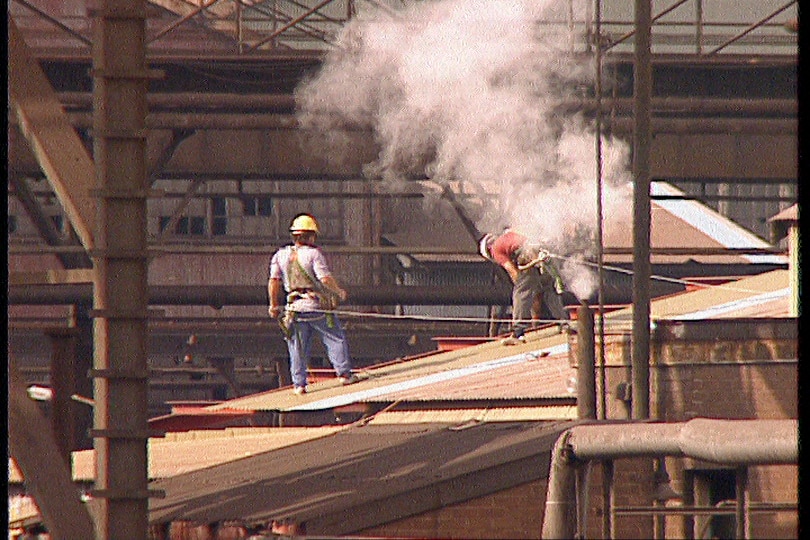an archival image of two men, dressed in high vis clothes, working at an industrial site