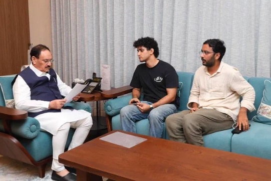 Three men sit on blue sofas around a coffee table.