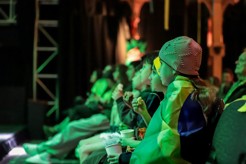 A seated row of children in the green glow of a large television projector