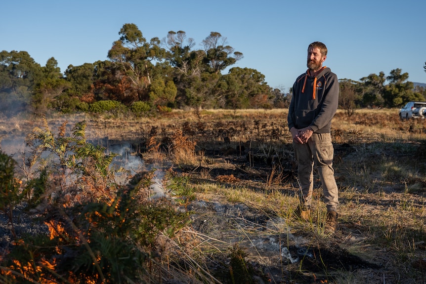 A man watches on as fire burns a patch of vegetation.