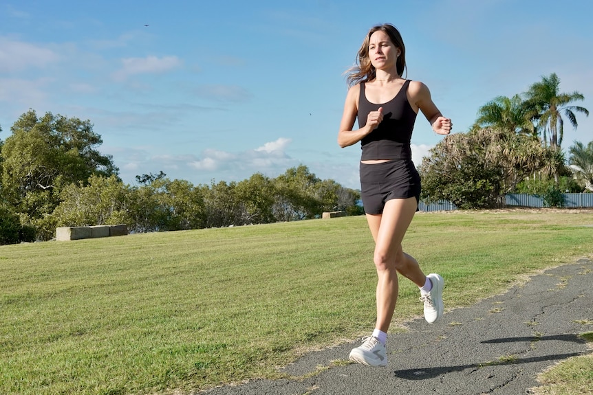 A woman running on a path next to grass and trees.