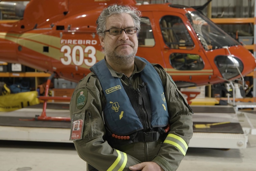 A man wearing a flight uniform stands in front of a helicopter.
