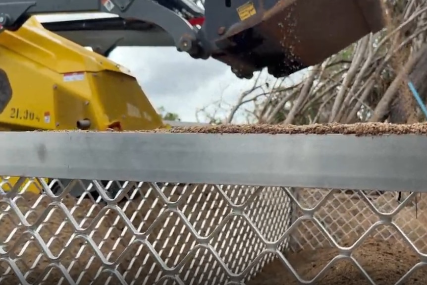 An excavator pouring sand into a cage