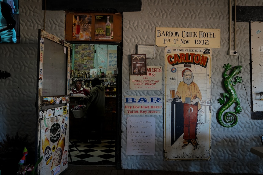 An open door leads into an outback pub, with signs reading 'WATERING HOLE' and 'BARROW CREEK HOTEL'.