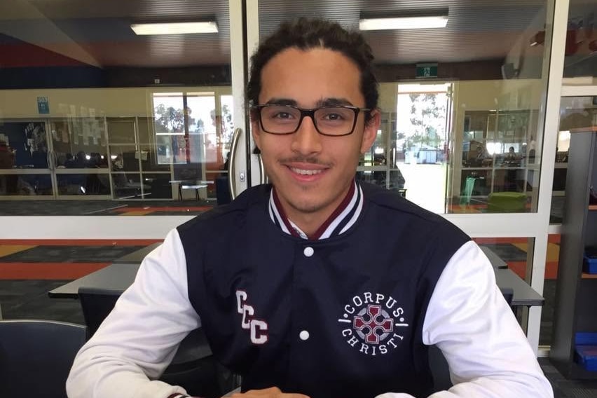 A boy who wears senior high school uniform sits at a desk.