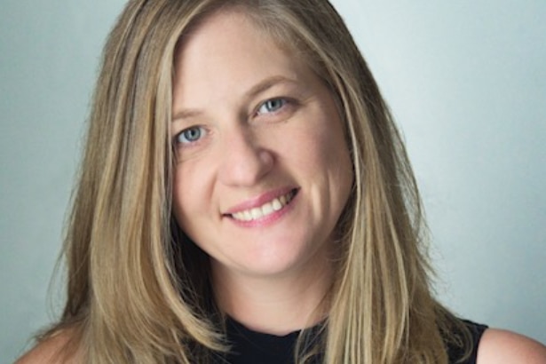 Nina with long blonde hair smiles at the camera. A headshot with a blank background.