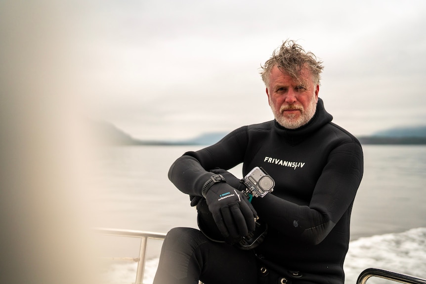 A man in a wetsuit on a boat looking at the camera