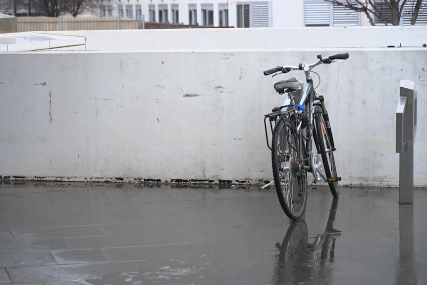 A lone bike at a bike rack on a rainy day.
