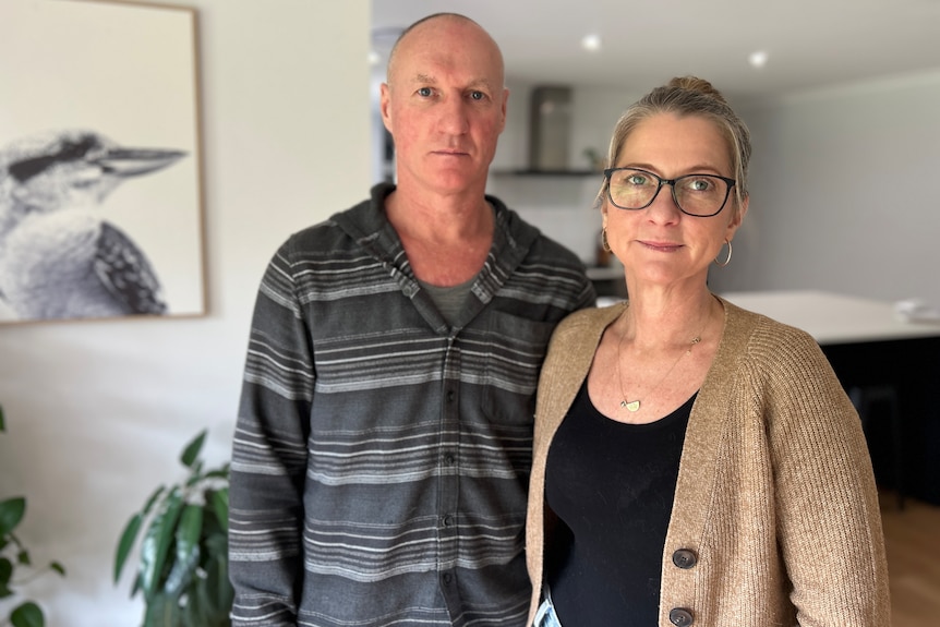 A mid-shot shot of a man and a woman posing for a photo standing up inside their living room.