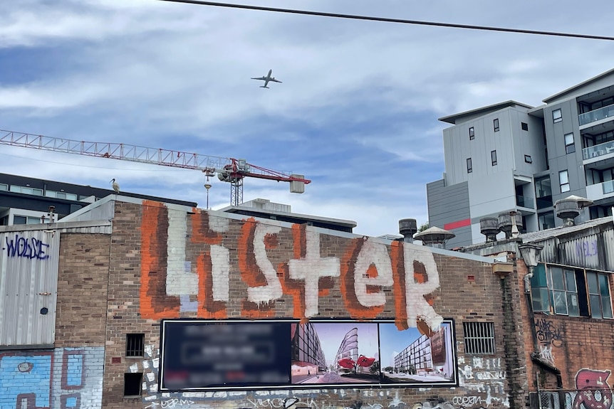 Anthony Lister tag on an old building in Lewisham saying 'Lister' clouding sky and plane flying in the background