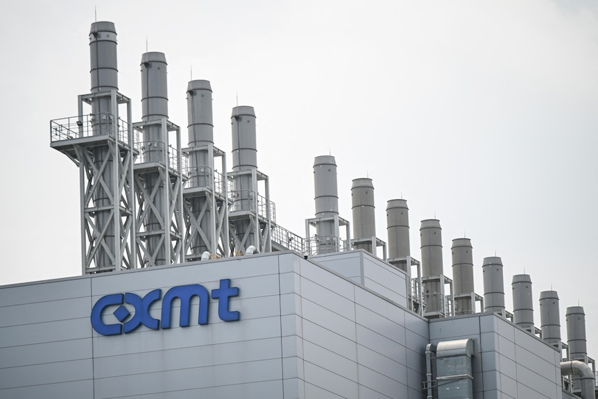 A row of 13 chimneys on the roof of a building with a blue logo saying "CMXT".