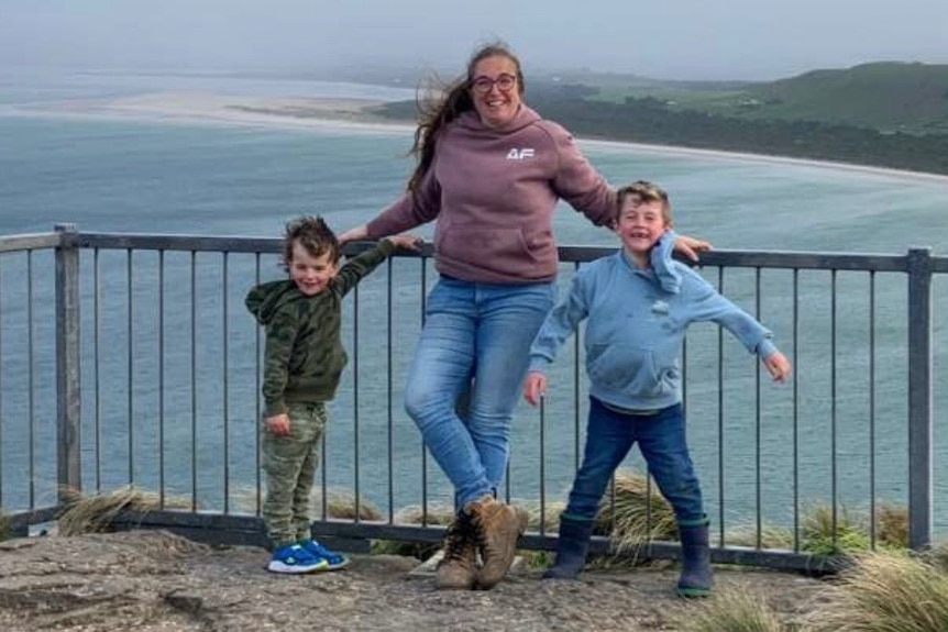 A woman posing with two young boys at a lookout over the ocean.