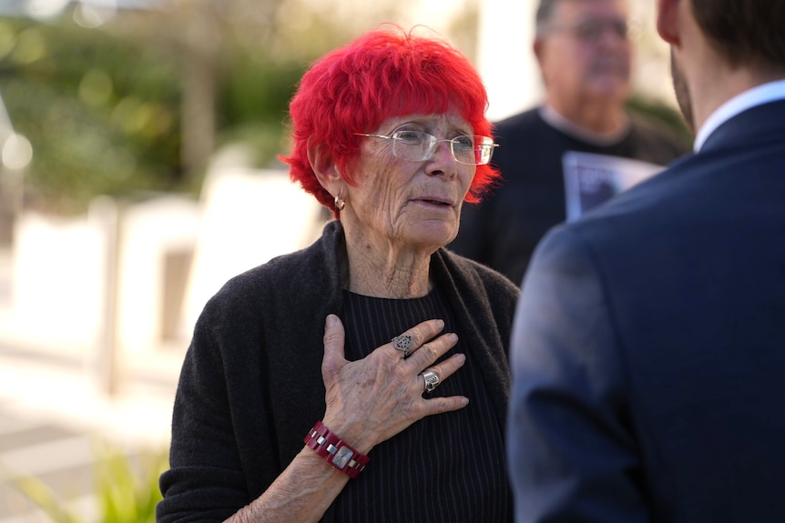 A woman with red hair wearing glasses and dressed in formal attire.