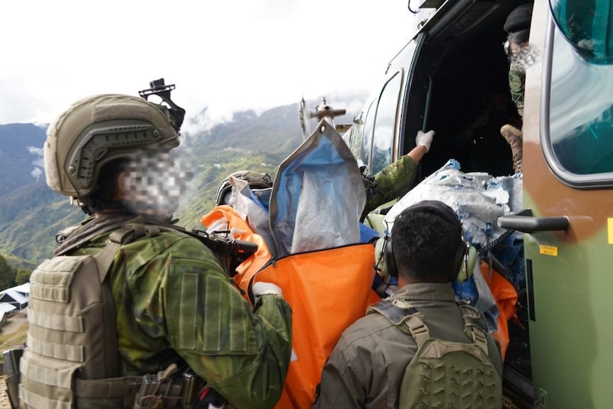 Soldiers in uniform load a dead body onto a helicopter.