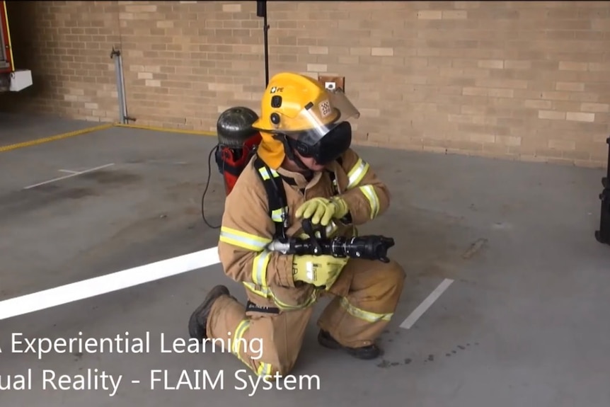 A CFA volunteer dressed in firefighting uniform, using a VR headset and a VR hose, pointing it in a direction, in a brick room