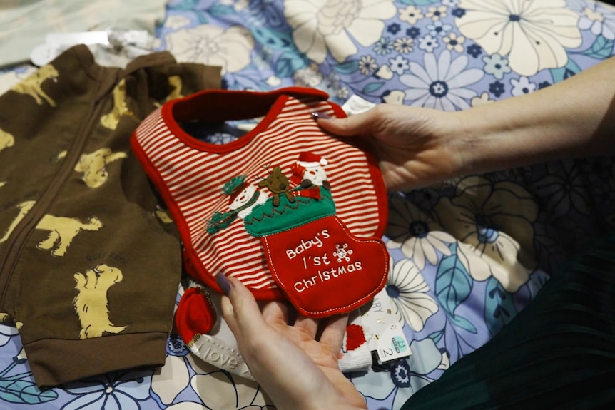 A woman holding a baby's Christmas-themed bib in her hands.