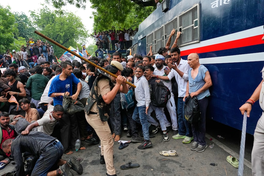 A man with a baton swings it at about a dozen men.