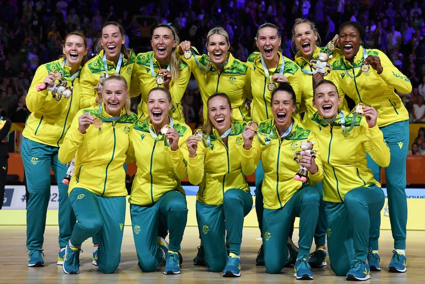 Australia players in green and gold tracksuits pose for a team photo smiling and holding medals out from around their necks.