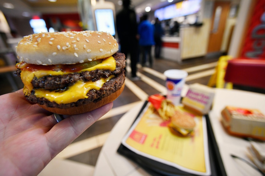 A hand holding up a burger with cheese, pickles, tomato sauce and beef inside it.