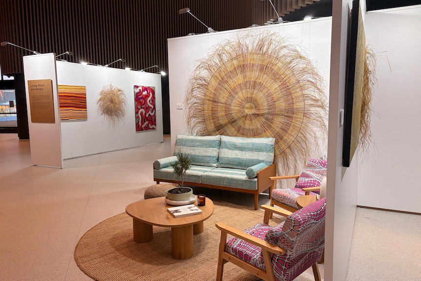 A wide shot of a gallery with artworks on the wall and colourful couches with art as print.