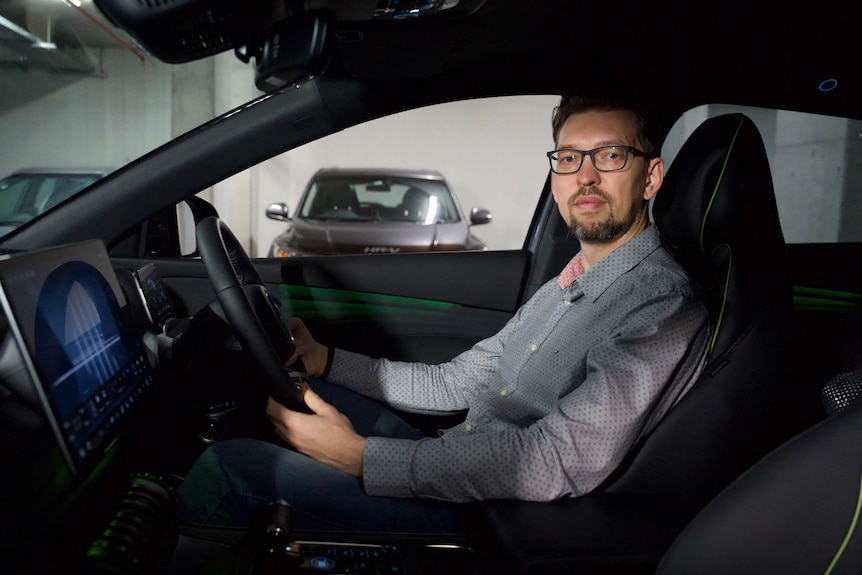 A man sitting inside a car at the steering wheel looking at the passenger sea