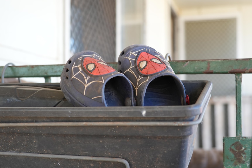 A pair of kids spiderman crocs sitting in an empty flowerbox hanging on a porch rail