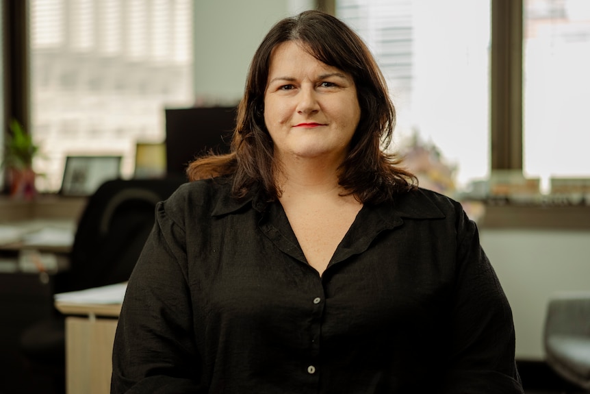 A woman wearing black sitting in an office with a window in the background
