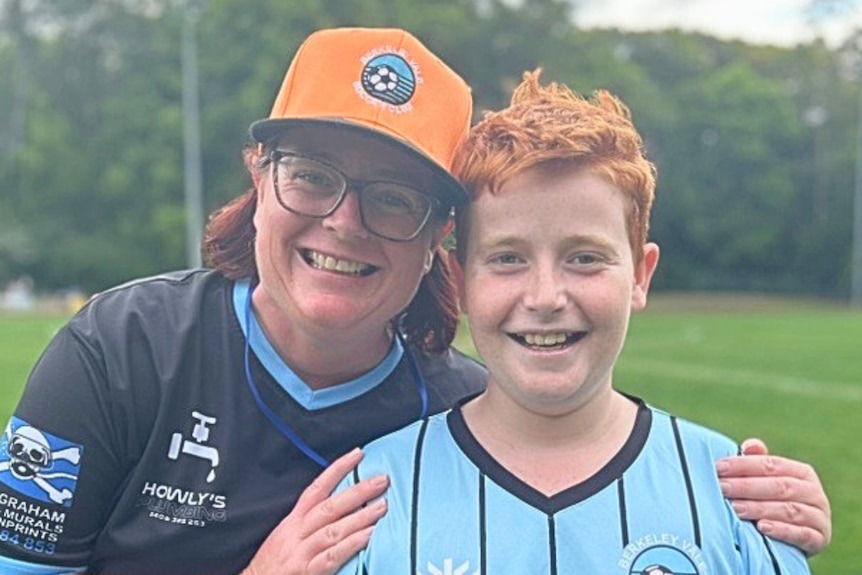 A woman standing with her arms around a boy. They are both wearing team jerseys.