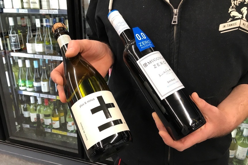 two bottles of zero-alcohol wines being held in the hand of person in abottle shop