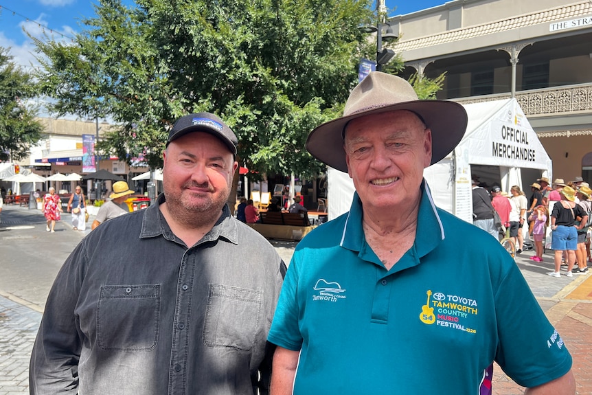 A middle-aged man in a cap and an older man in an Akubra stand on the street in a country town.