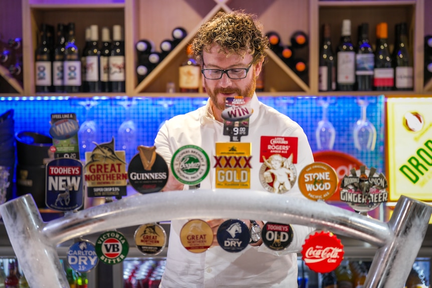 A man working behind a bar with a range of beers on tap in front of him.
