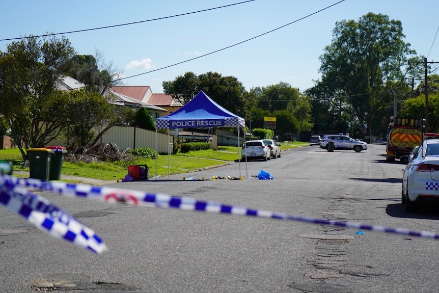 A wide shot of a street cordoned off with police tape with police tent in the background