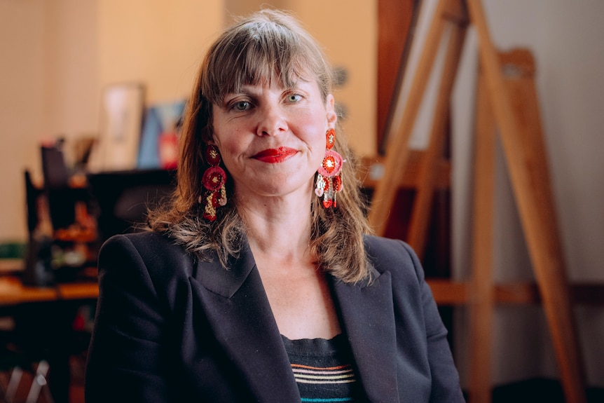 A woman with red earrings and red lipstick looks into the camera.