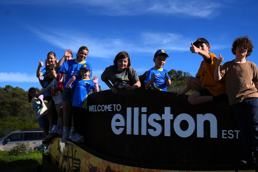 Children smile at the camera at the welcome to Elliston sign