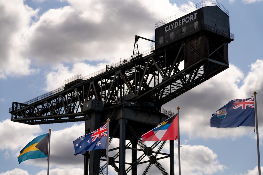 Flags of Bahamas, Australia, Antigua and Barbuda, and Anguilla in front of the Finnieston Crane on Glasgow's Clyde River.