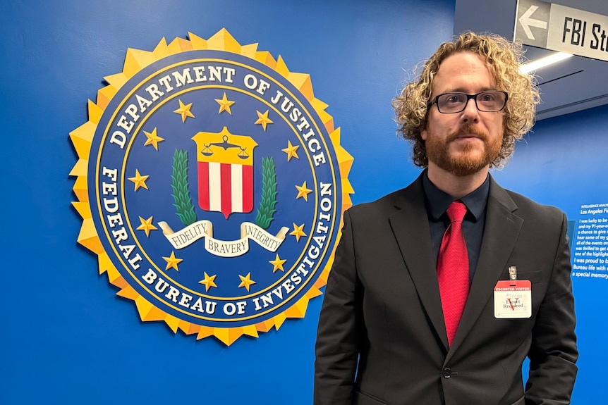 A man in a black suit standing next to a large sign for the FBI.