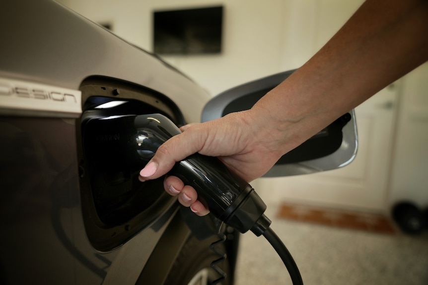 A woman's hand holds a charging jack to an electric vehicle.