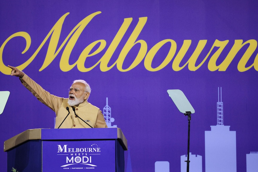 A man stands behind a lecturn gesturing with his arm.