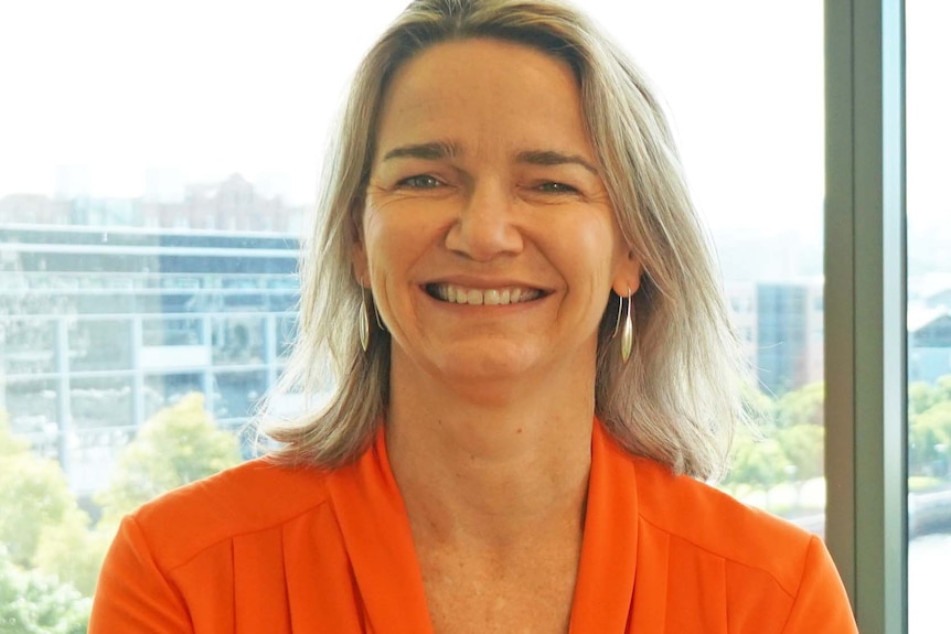 A smiling woman in an orange jacket.