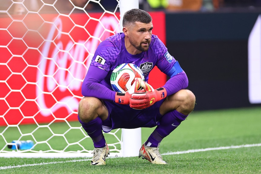 Mat Ryan holds the football while crouching and looking disappointed