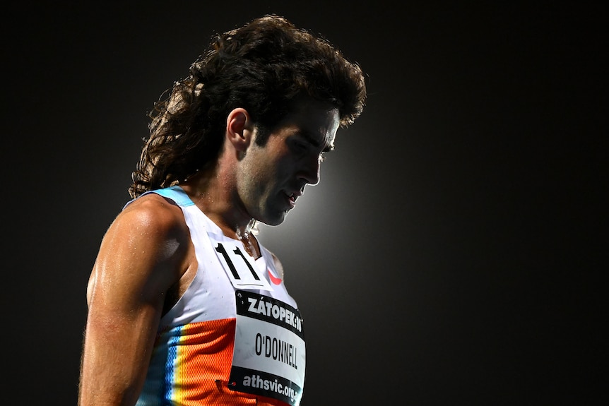 Seth O'Donnell stands on an athletics track with a light behind his mullet.